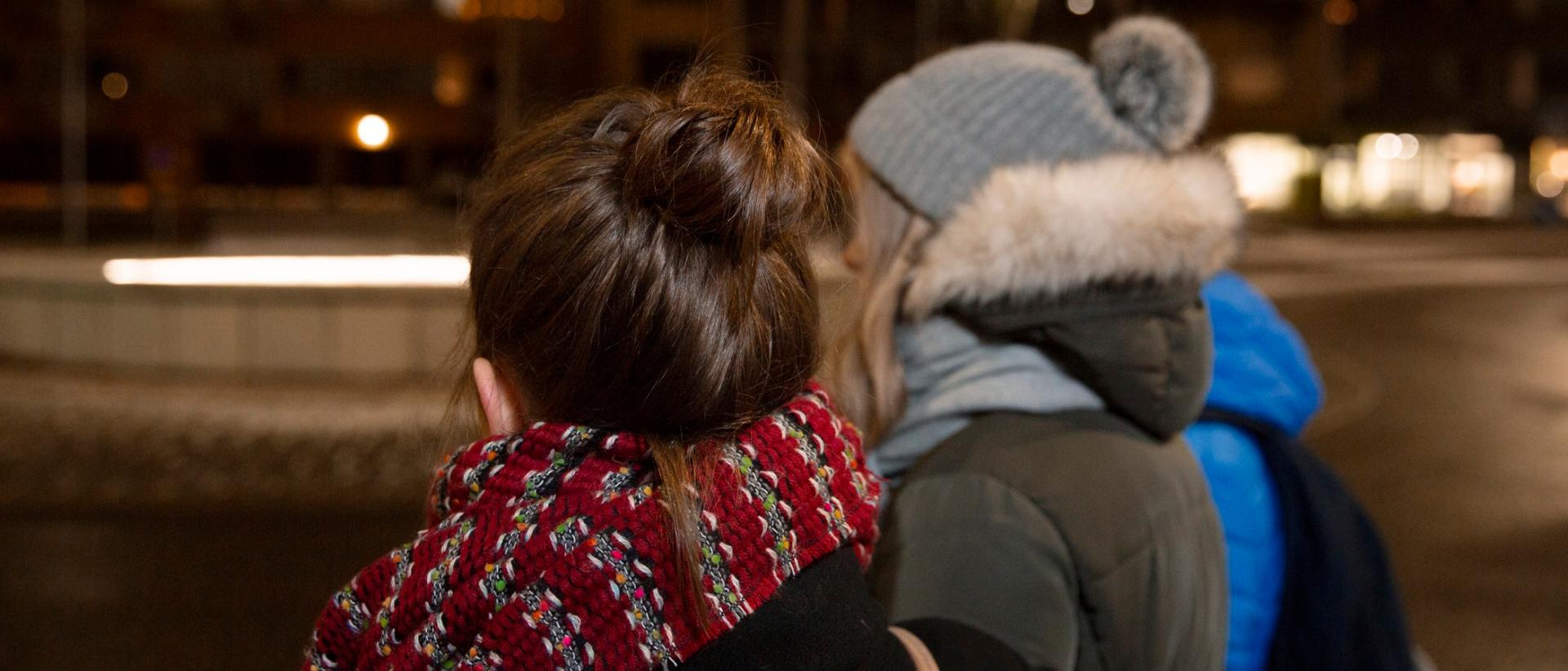 Kaksi teinityttöä selin ulkona talvihämärässä