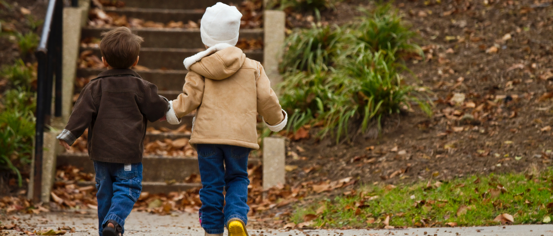 Kaksi lasta kävelemässä portaita kohti käsi kädessä syksyisellä säällä.
