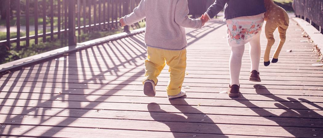 Sillalla käsi kädessä juoksevia lapsia, keväinen ilma ja auringonpaistetta.