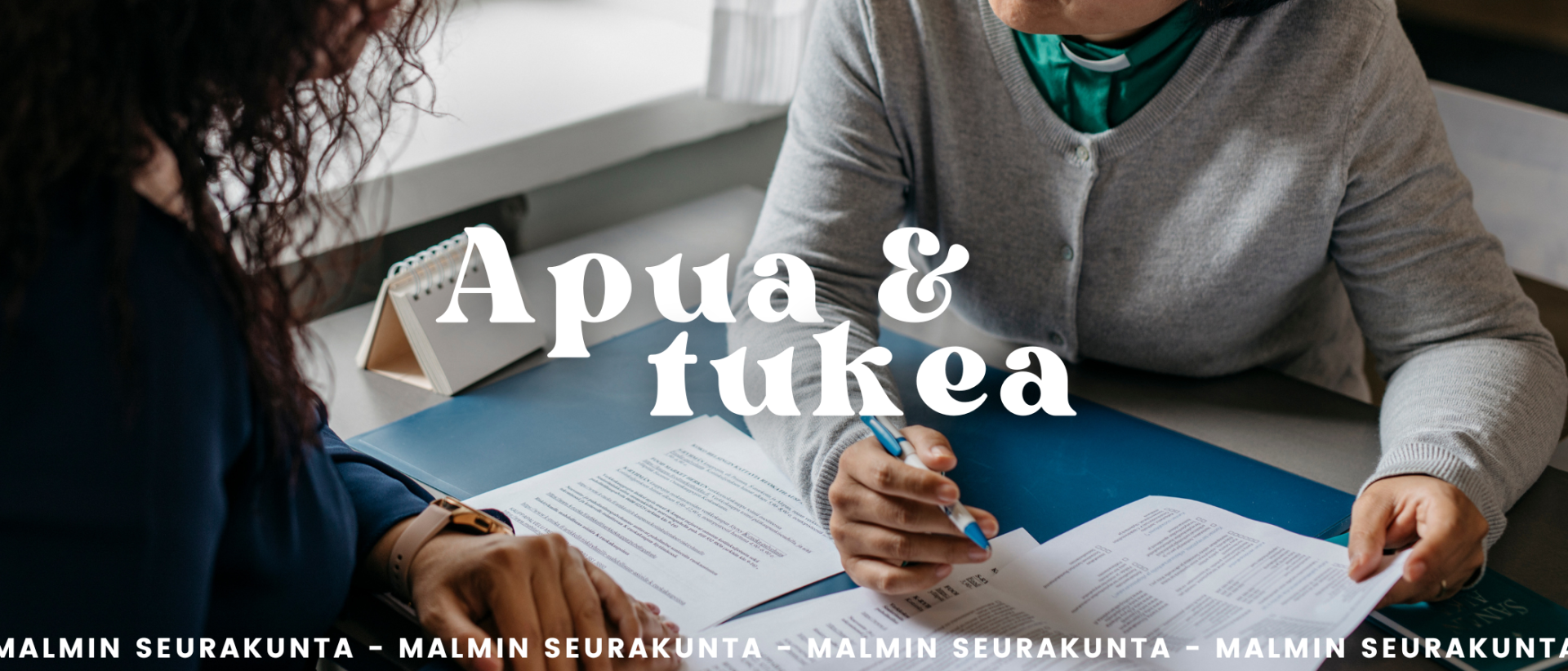 Apua ja tukea Malmin seurakunta, kuvassa kaksi ihmistä työpöydän molemmin puolin, täytetään papereita