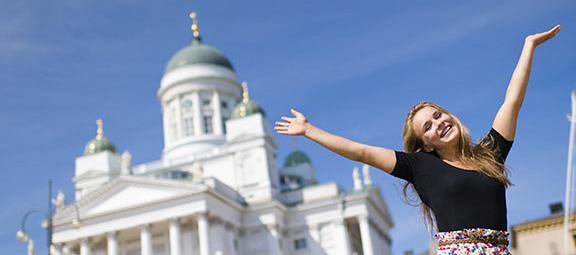 Kuvassa Helsingin tuomiokirkko ja sen edessä iloinen tyttö kädet ylhäällä