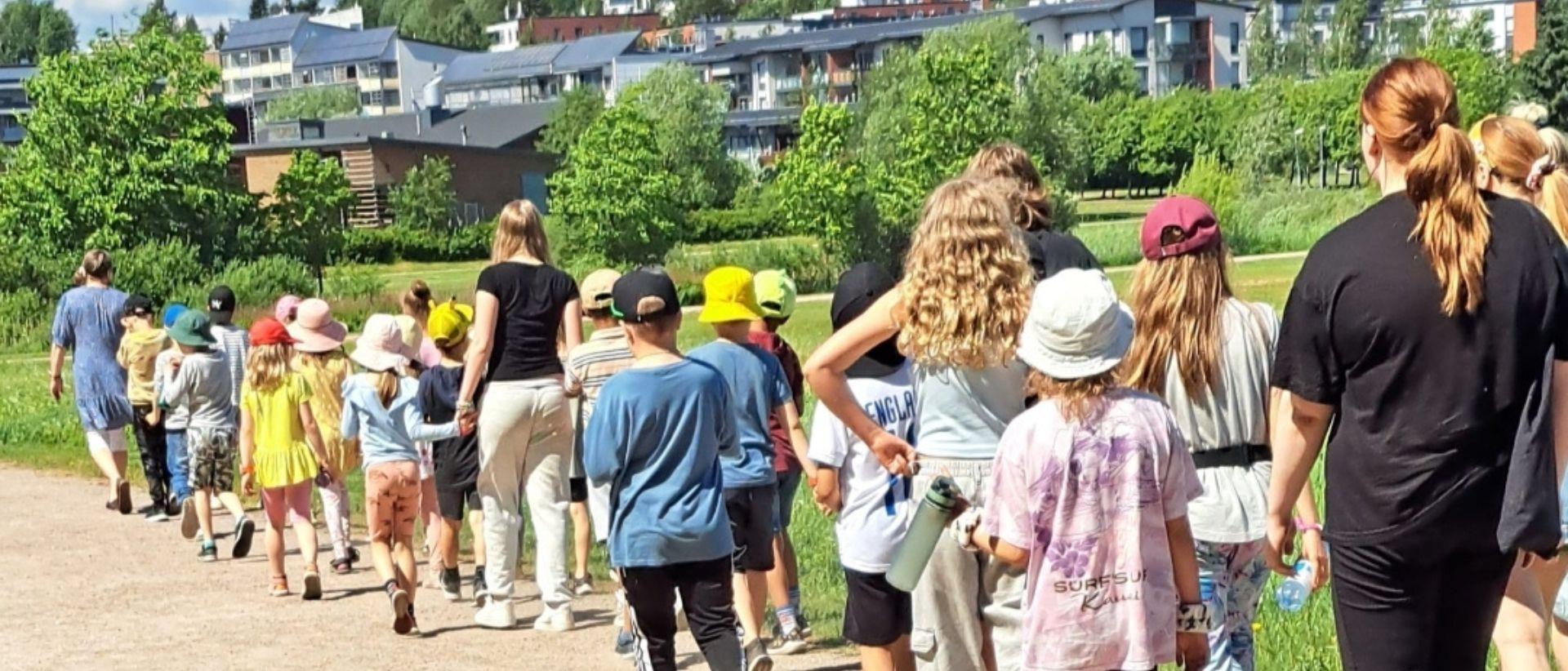 Koululaisia kävelemässä ohjaajien kanssa kesäisessä Viikissä