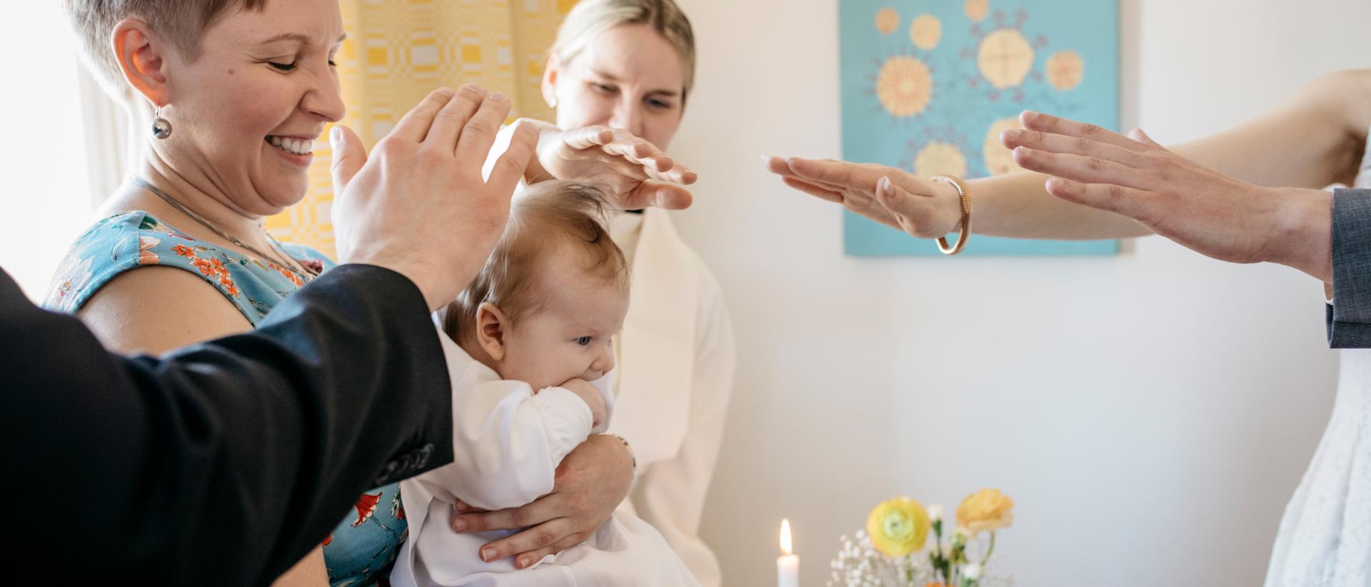 Kummit siunaamassa vauvaa kotikasteella kädet kohotettuina. Kuva Elina Manninen.