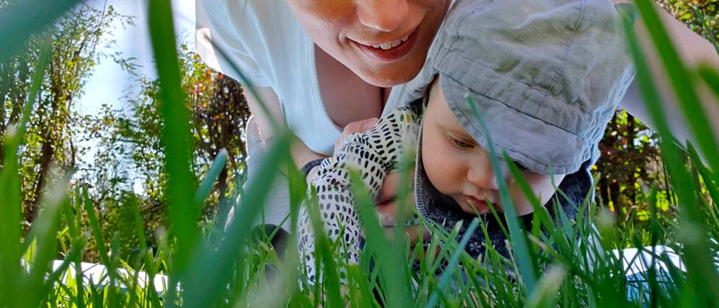 Vauva äitinsä kanssa tutkii kontallaan ruohikkoa.