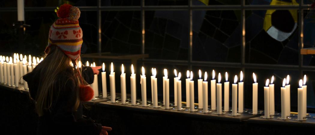 Vainajien muistokynttilät Kannelmäen kirkon alttarikaiteella, pipopäinen tyttö seisoo kynttilöiden vieressä.
