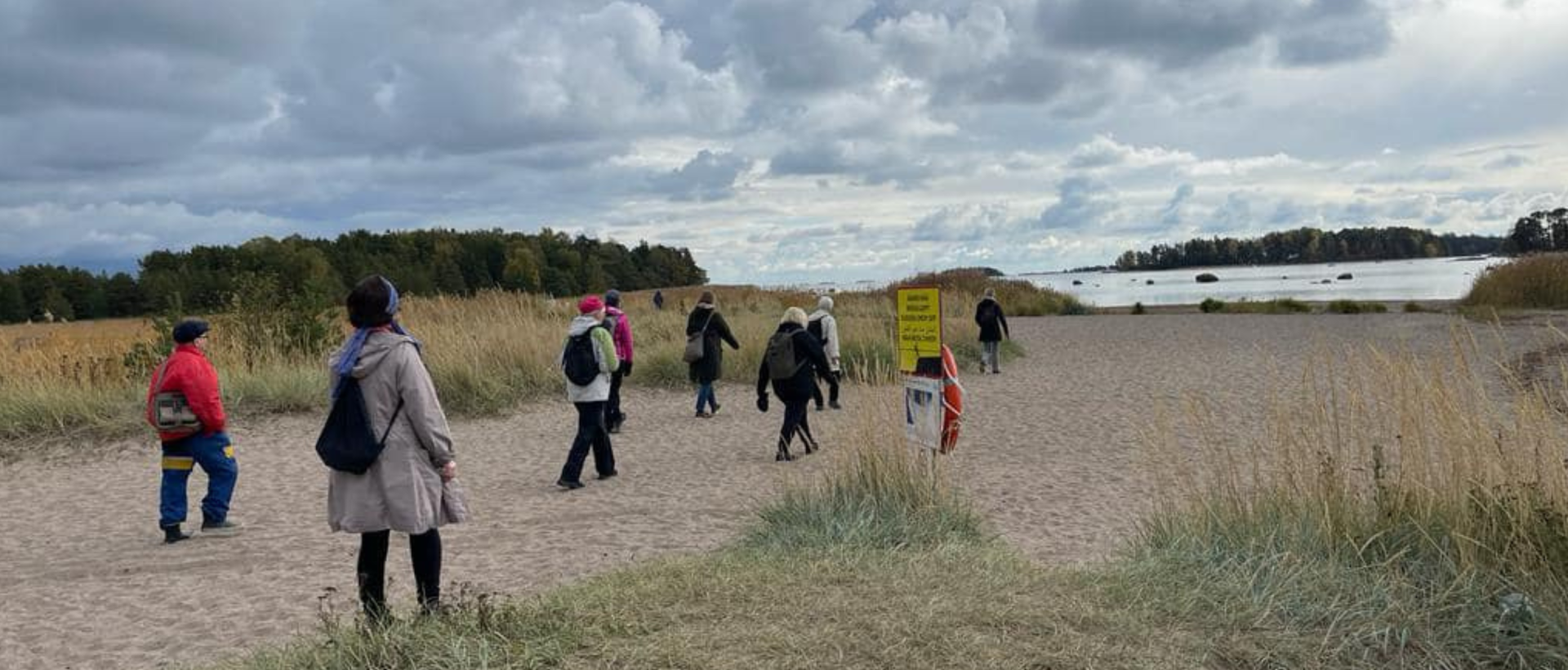 Pyhiinvaeltajia rannalla Itä-Helsingissä. Hiekkamaata, taivaalla kumpuilevia pilviä