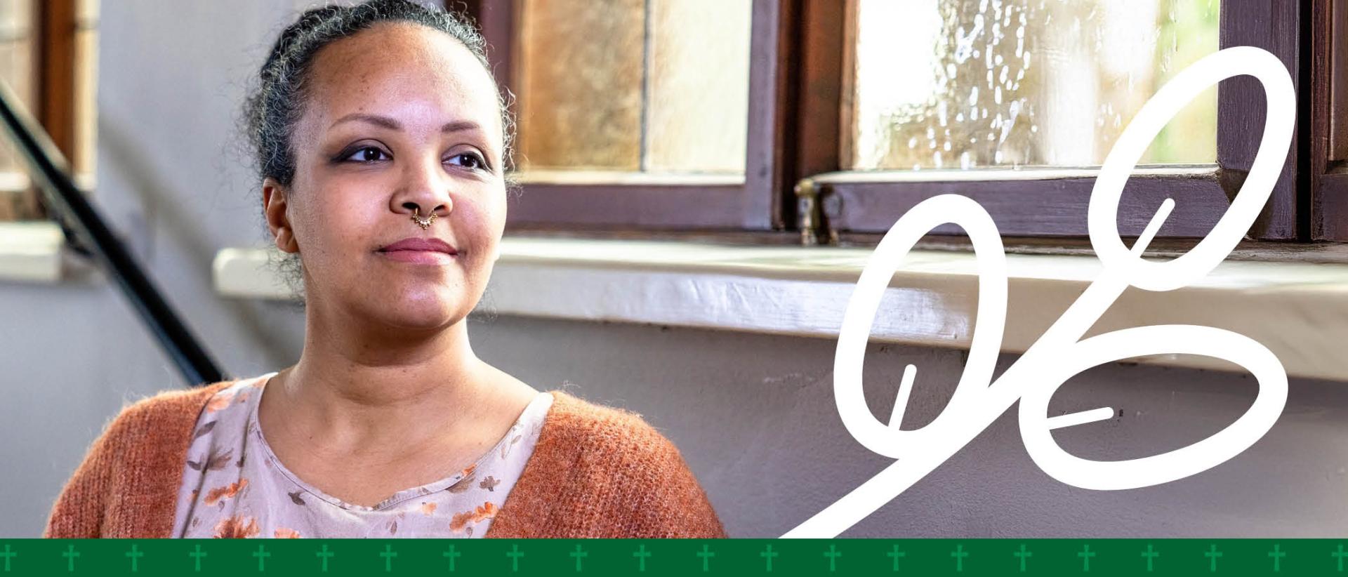 Tummahiuksinen nainen istuu penkill&auml; ikkunan edess&auml; ja katsoo hymyillen