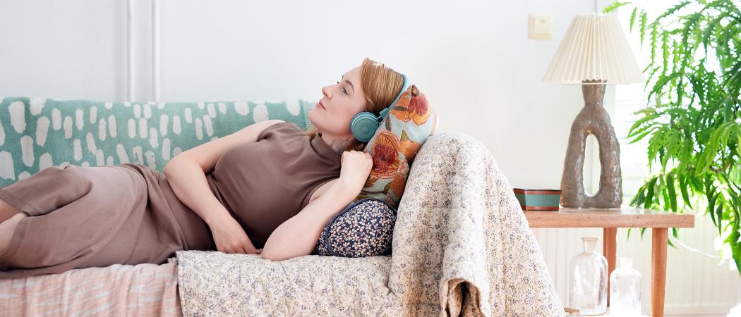 Nainen makaa sohvalla ja kuulokkeet päässään.