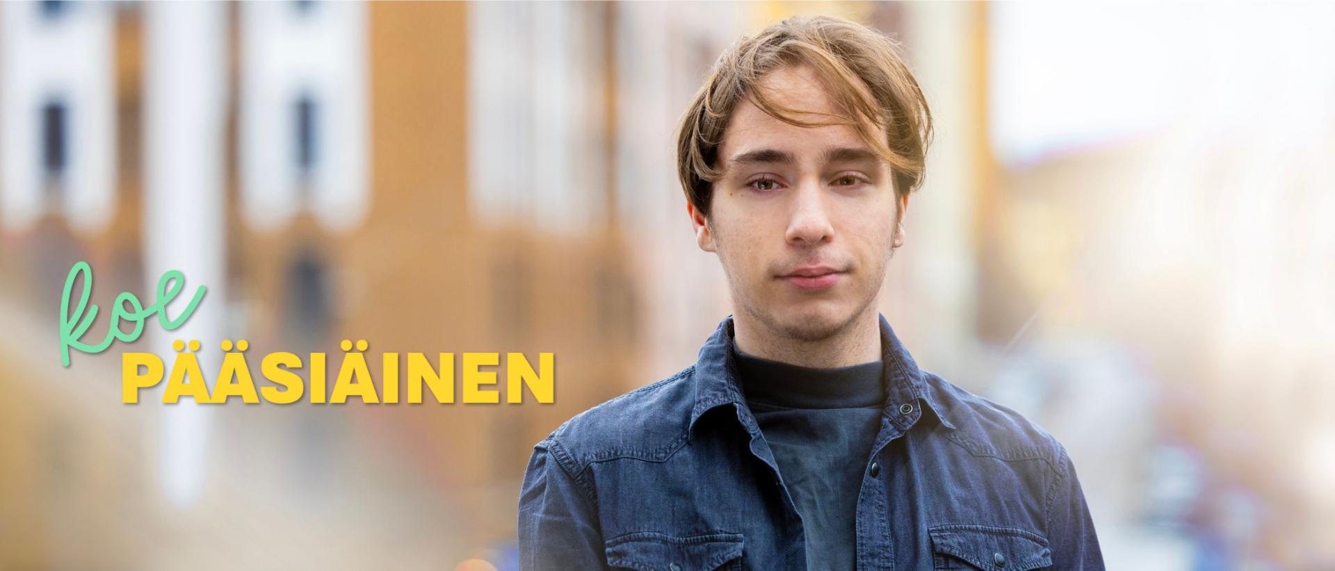 Nuori mies seisoo ulkona, päällään sininen pusero ja takki