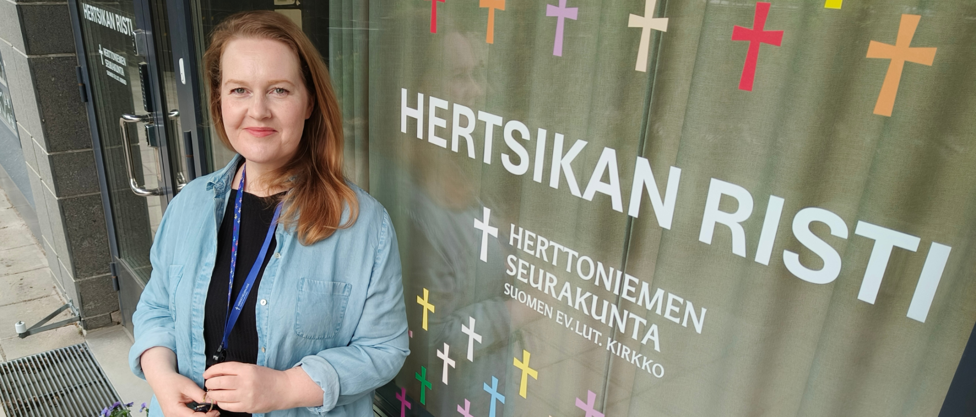 Diakoni Niina Marjanen Hertsikan ristin edessä vaaleansinisessä paidassa