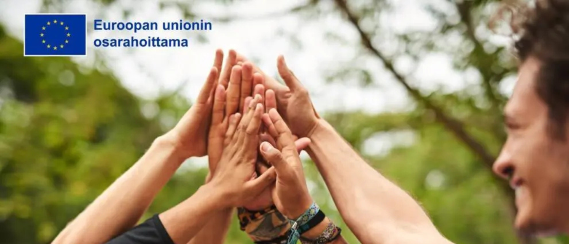 Joukko ihmisten käsiä yhteen ojennettuina kesäisessä maisemassa