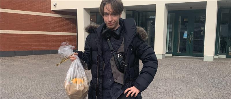 Henkilö seisoo pihalla toppatakki päällä kukkakimpun kanssa ja hymyilee.