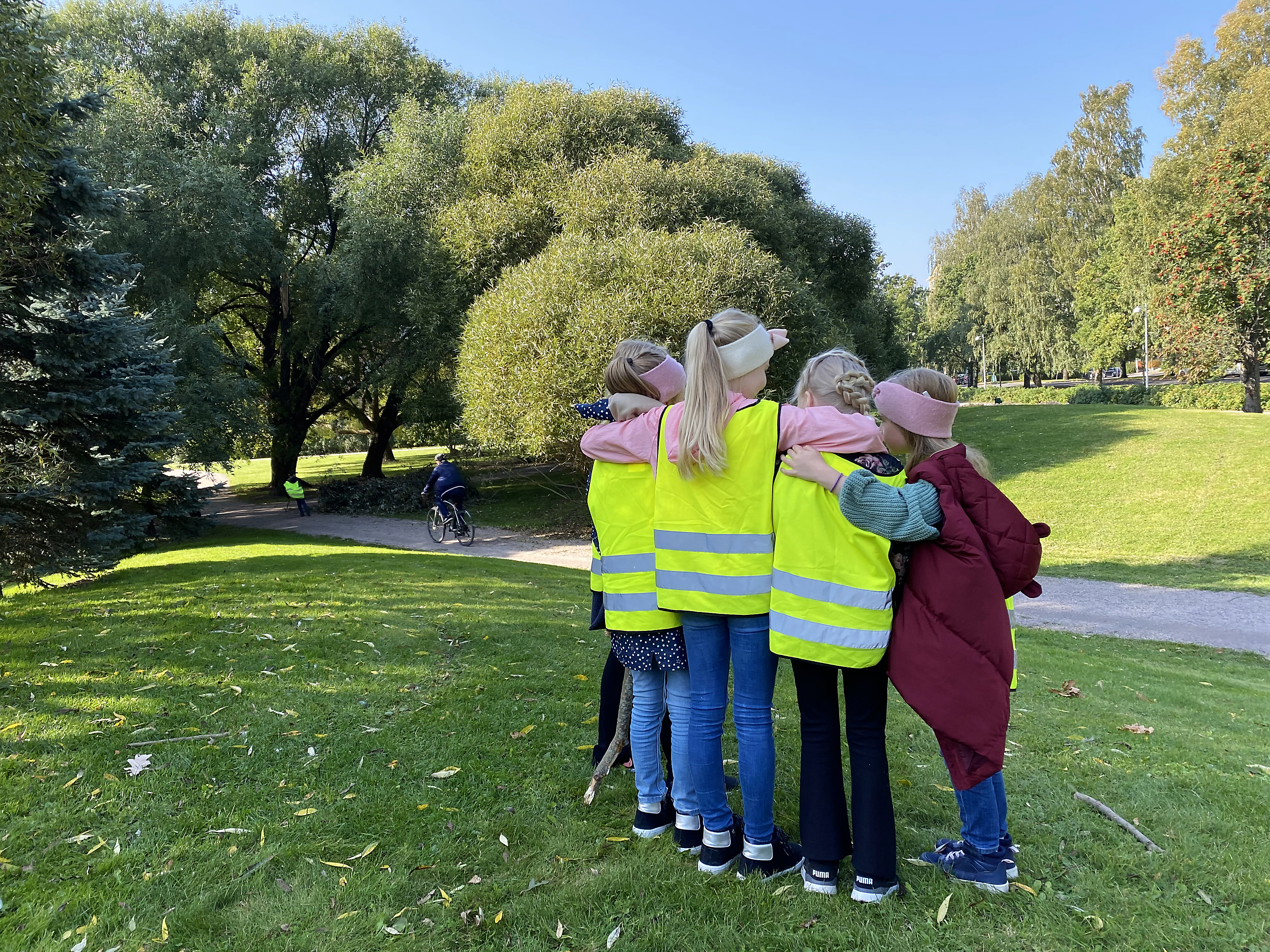 Fyra barn i reflexvästar står på led och håller armarna om varann med ryggarna vända mot kameran.