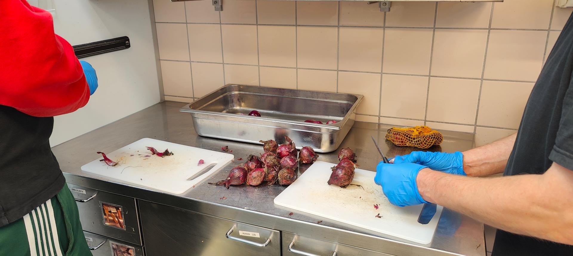 Kahden henkilön kädet, jotka leikkaavat keittiön työpöydällä sipulia