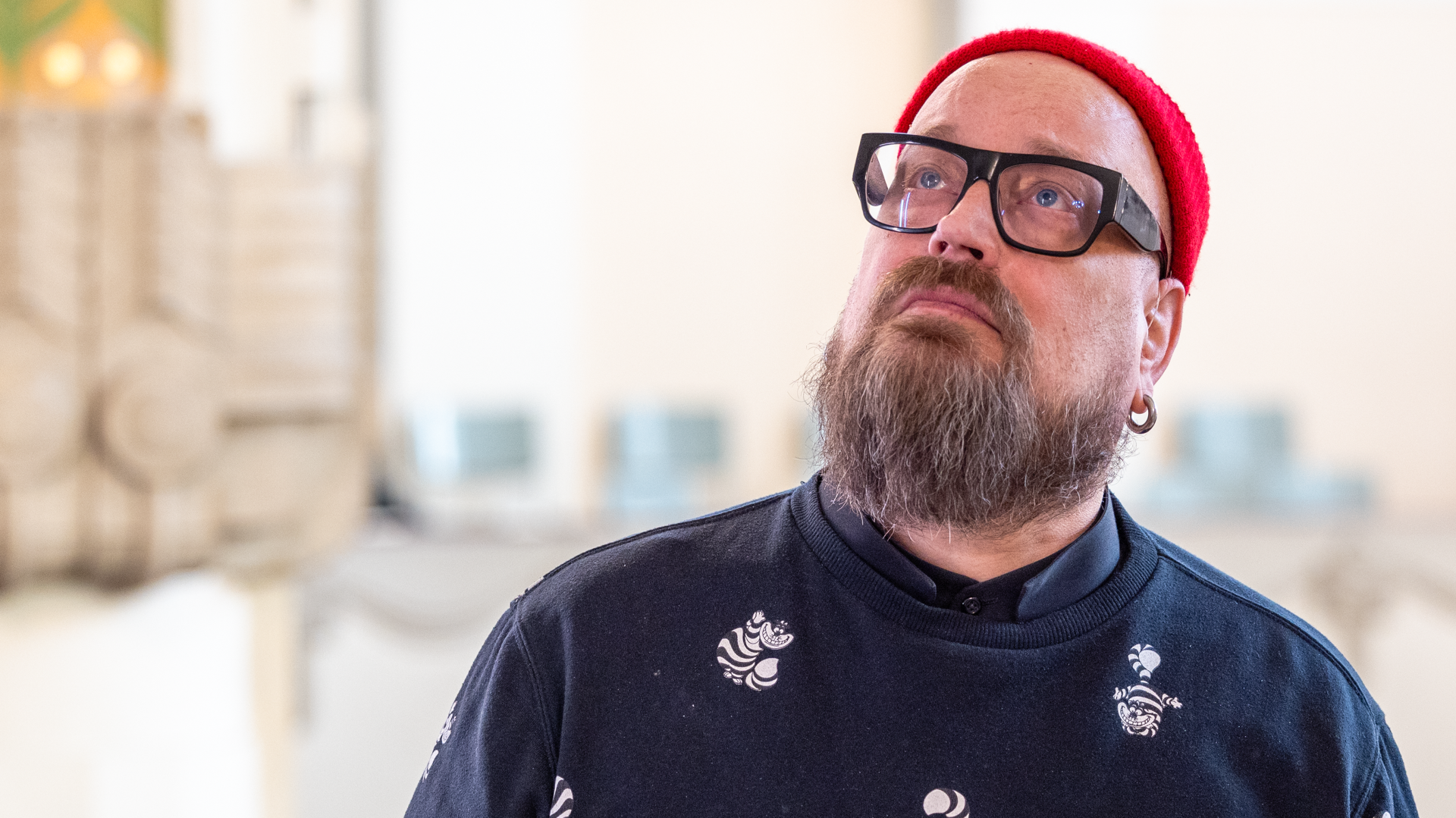 En man i röd, stickad mössa. Hans min är fundersam.