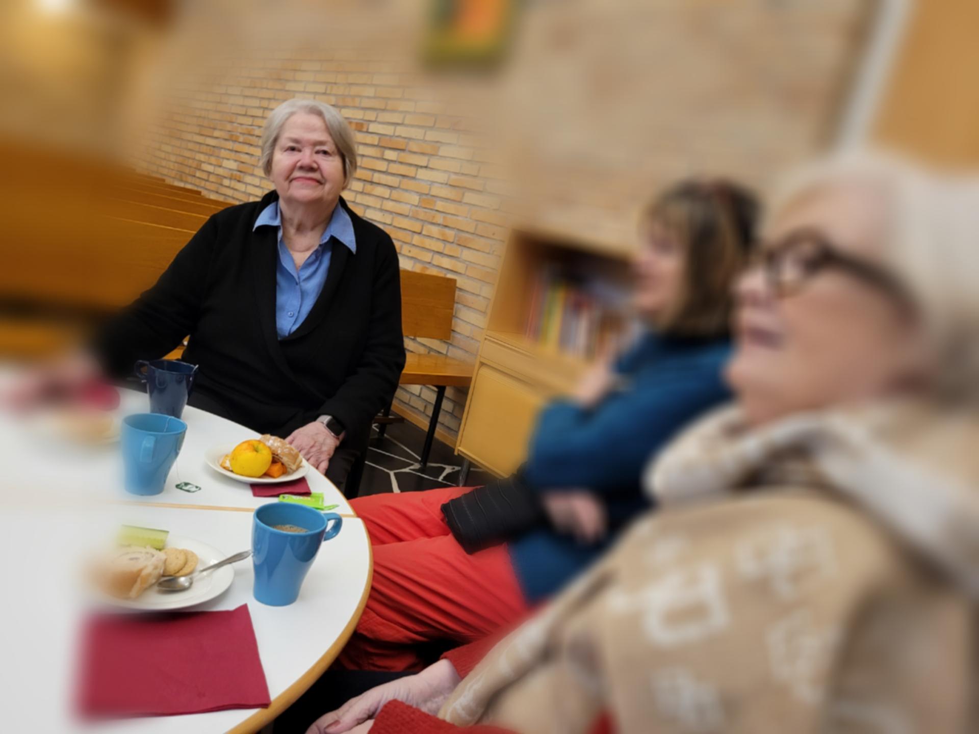 Tre kvinnor som sitter vid ett bord och dricker kaffe tillsammans.