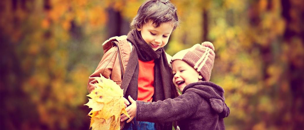 Kaksi lasta syksyisessä puistossa keltaisia vaahteranlehtiä käsissään.